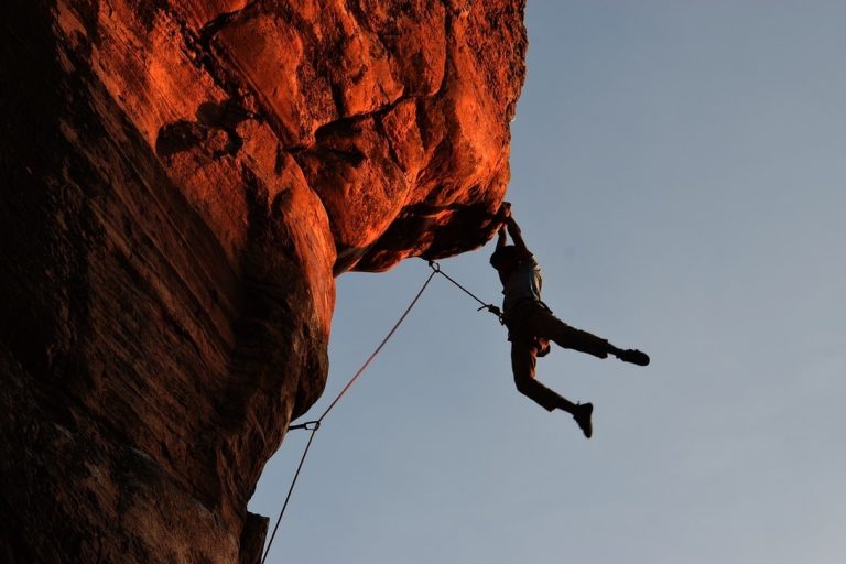 Male climber hanging from a cliff at sunset