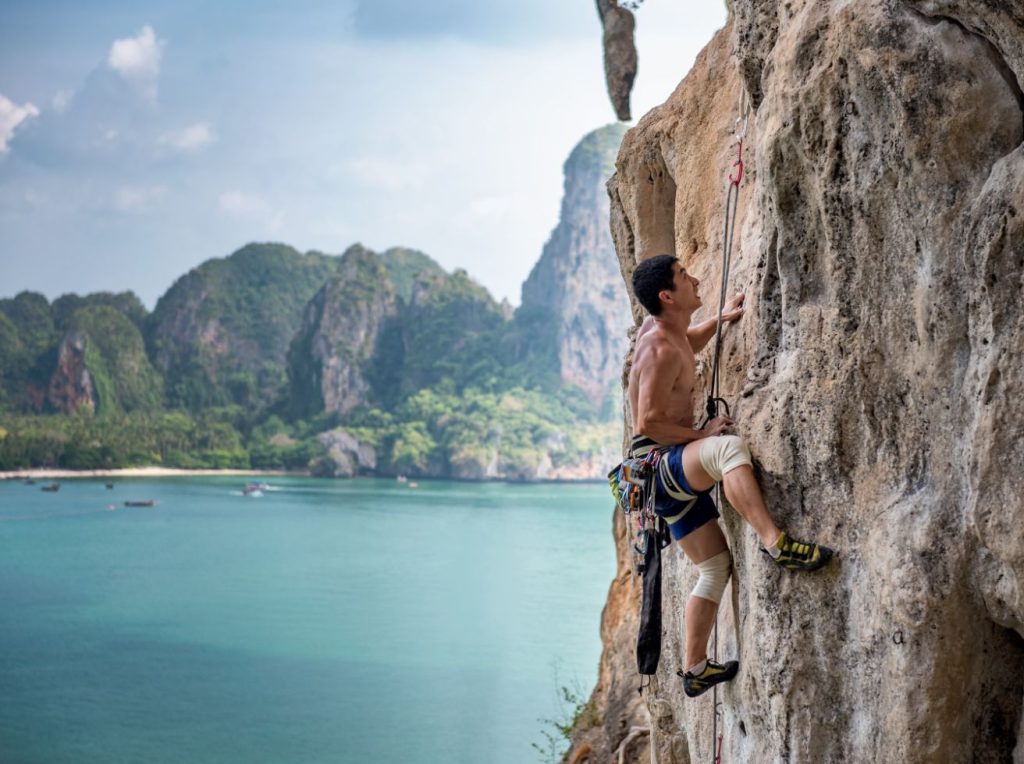 a man climbing a wall above water using sport climbing gear