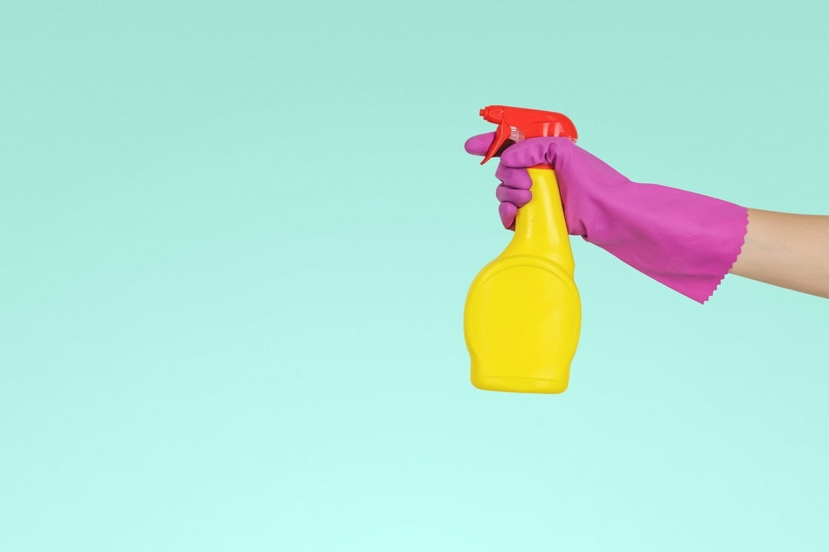 lady with hot pink gloves holding yellow cleaning bottle on light blue background.